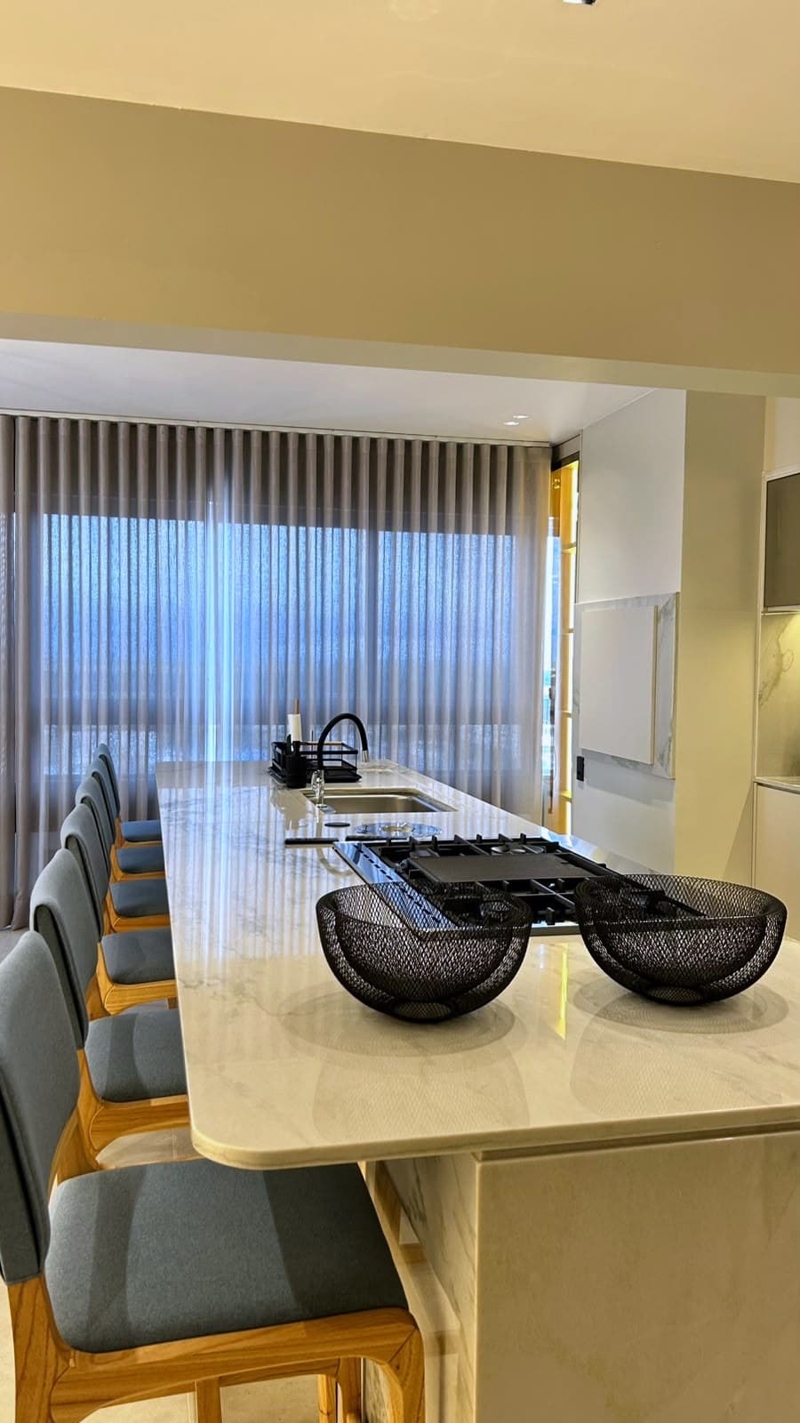 Bancada da cozinha em mármore com cooktop e cortina sheer ao fundo